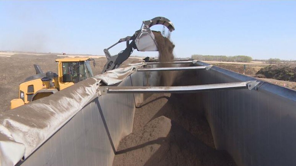 En traktor häller en spade kompost i en semitrailer.