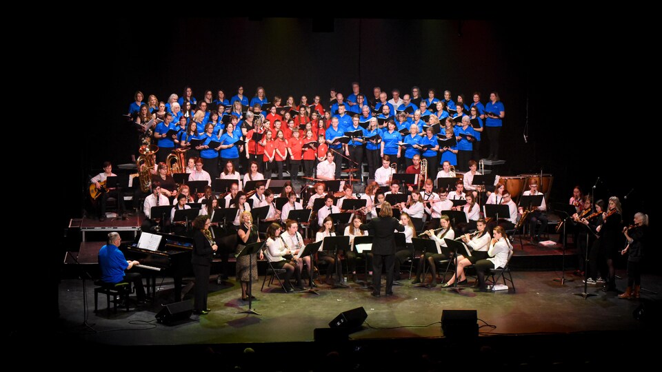 De nombreux chanteurs d'une chorale et des musiciens d'un orchestre symphonique en prestation sur scène.