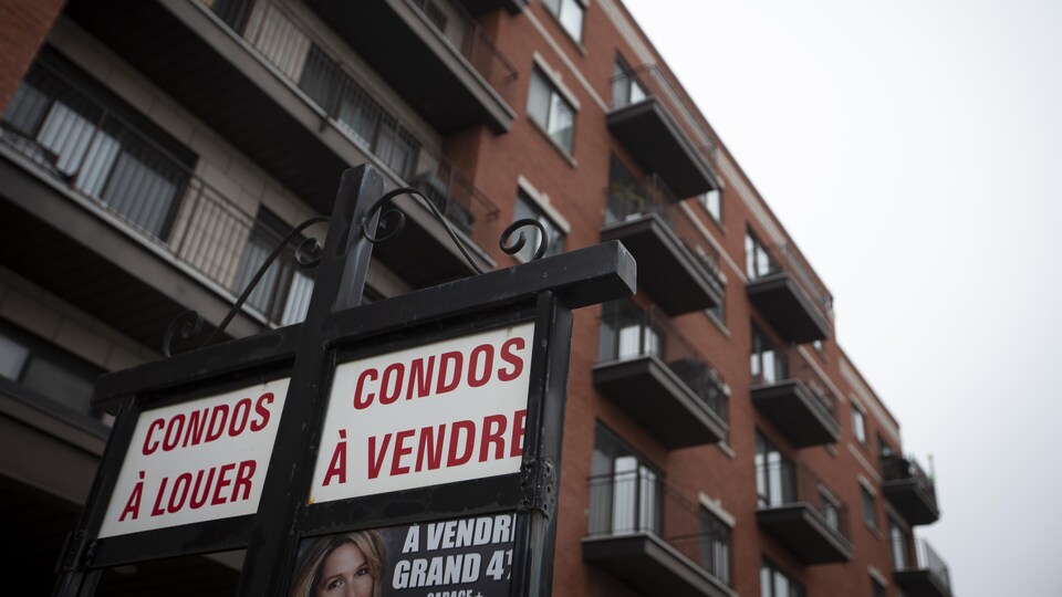 Pancarte indiquant des condos à vendre et à louer avec un édifice en arrière-plan.