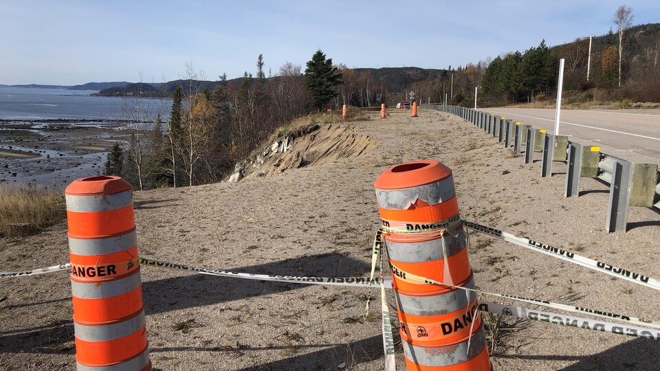 Des cônes orange, reliés par un ruban de sécurité, sont placés en bordure d'un talus affaissé près de route 138.