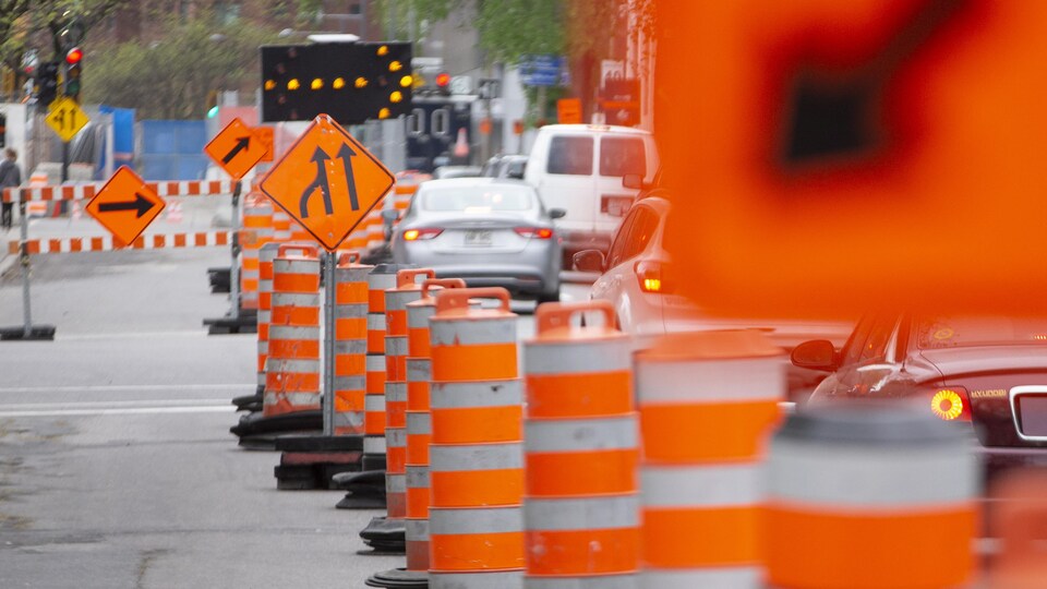 Des cônes orange, des panneaux et une flèche clignotante détournent la circulation près d'un chantier de construction.