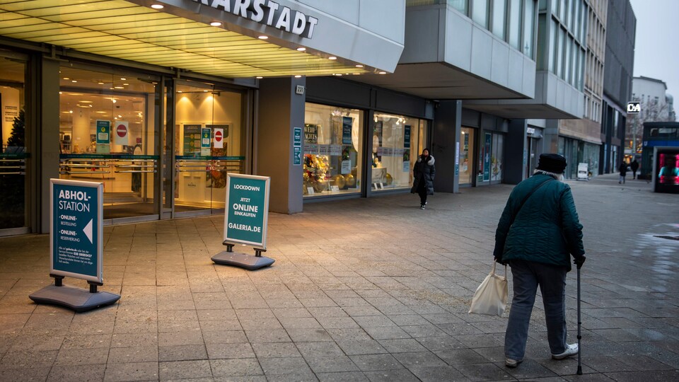 Une femme âgée marchant avec une canne passe devant un commerce.