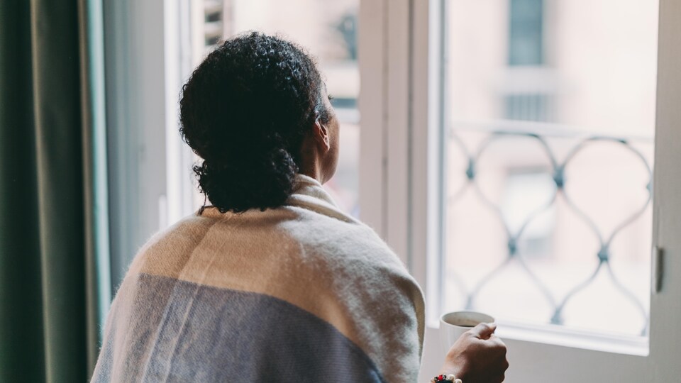 Une femme regardant par la fenêtre, un café dans la main.