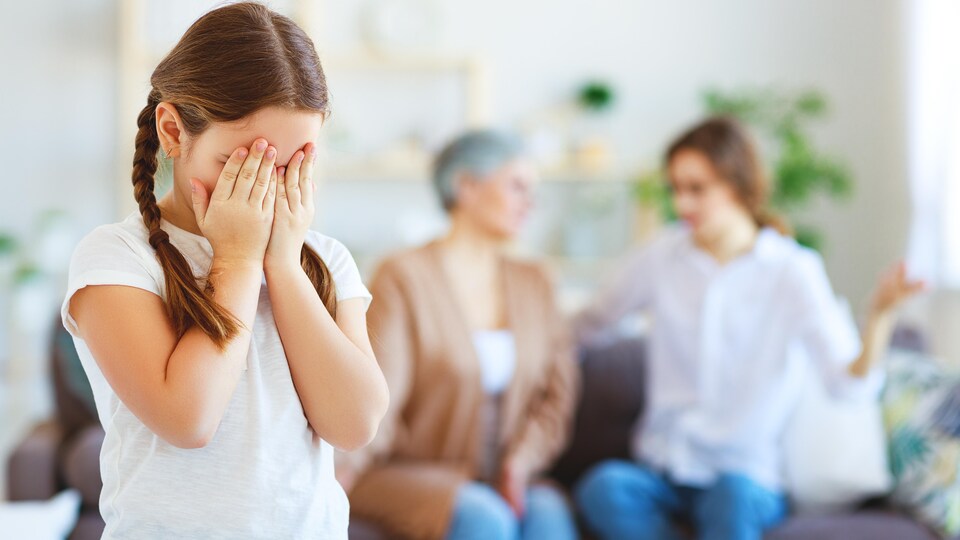 Une petite fille pleure alors que des adultes, derrière elle, discutent.
