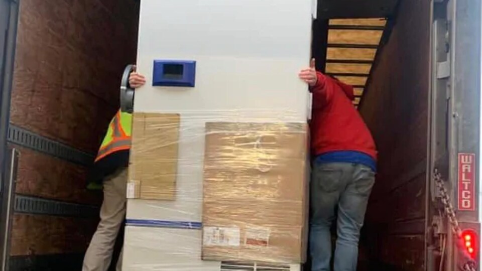 Deux personnes chargent un congélateur dans un camion.