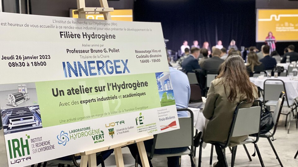 Une pancarte indiquant une conférence sur le sujet de l'hydrogène et des gens assis. 