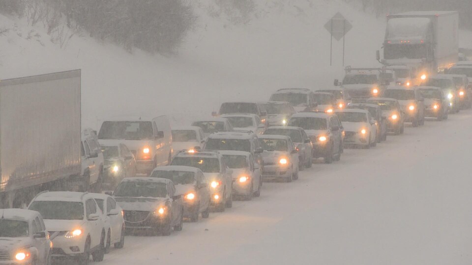 Deux rangées de voitures dans la neige sur une autoroute congestionnée.