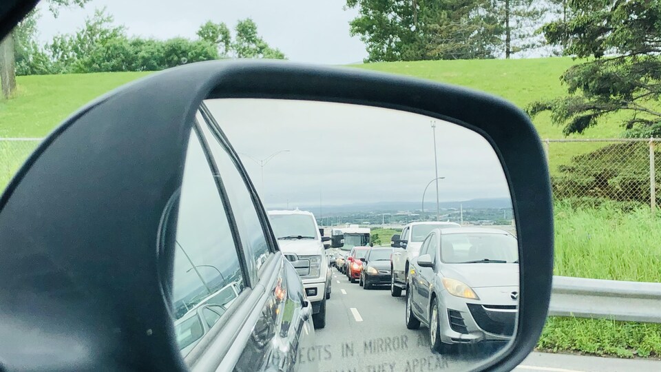 Gros plan sur un rétroviseur extérieur de voiture dans lequel on aperçoit une longue file de voitures les unes derrière les autres.