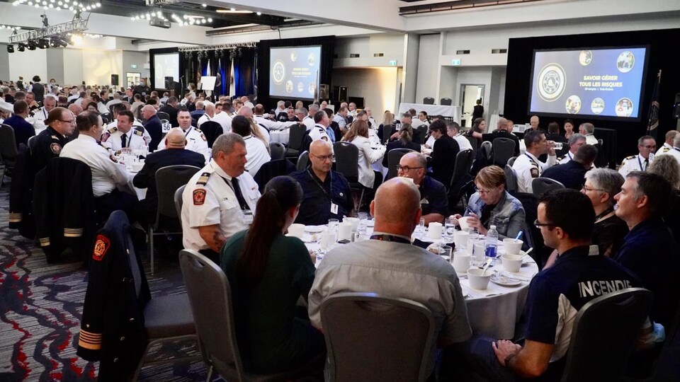 Des centaines de participants rassemblés par table de 10 personnes dans une salle bondée.