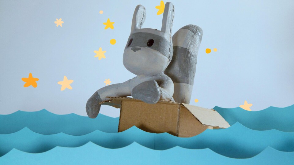 Un personnage de raton laveur en marionnette vogue sur des eaux en papier à bord d'une boîte en carton.