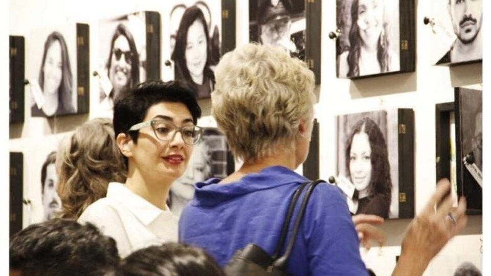 Maryam Hafizirad communique avec une femme lors d'une exposition. Derrière elles se trouvent des portraits accrochés sur un mur.