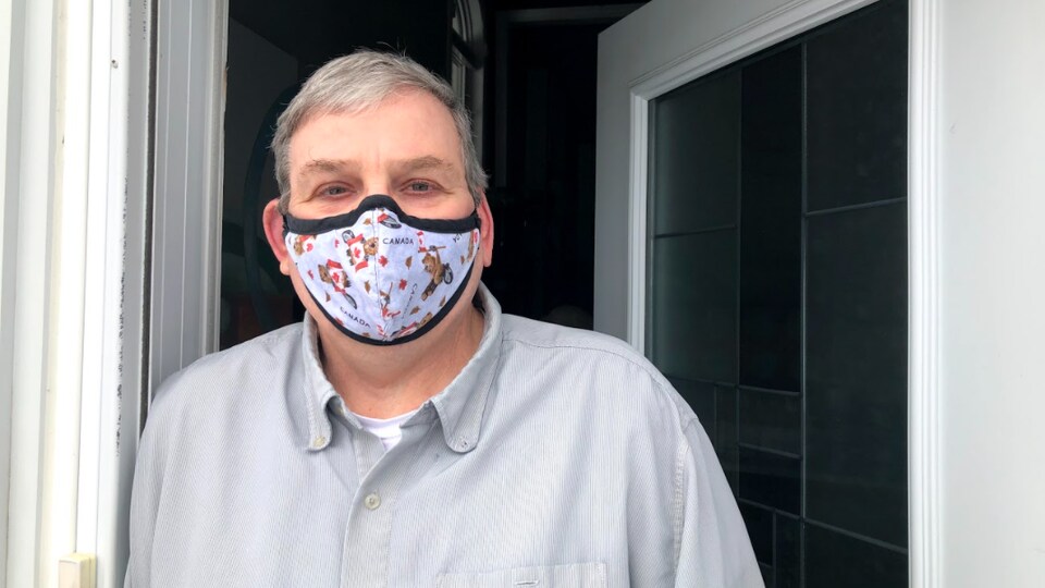 Conrad Tittley portant un masque dans un cadre de porte, regardant la caméra.