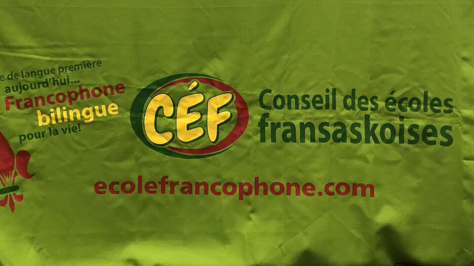 Une table aux couleurs du Conseil des écoles fransaskoises, avec le logo jaune et vert et rouge, ainsi que des éléments sur la table, comme une balance et un projecteur