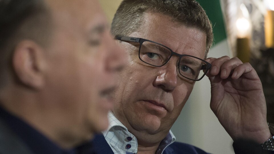 Scott Moe, pris de profil, en train de regarder François Legault qui répond aux questions des médias en conférence de presse.
