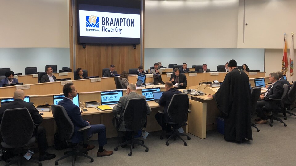 Séance au conseil municipal où un membre d'une délégation chrétienne s'exprime devant des conseillers municipaux.