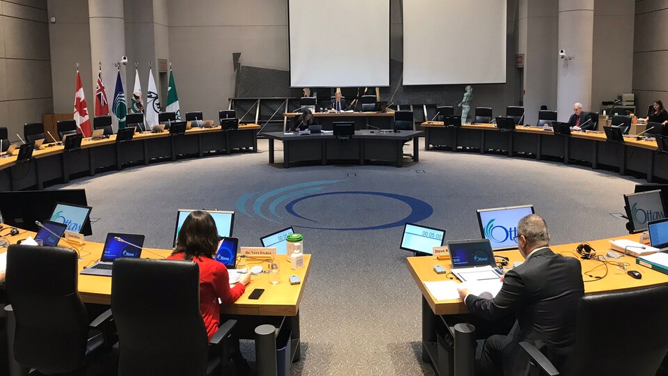 On voit le maire Jim Watson au bout de la table et plusieurs chaises vides.