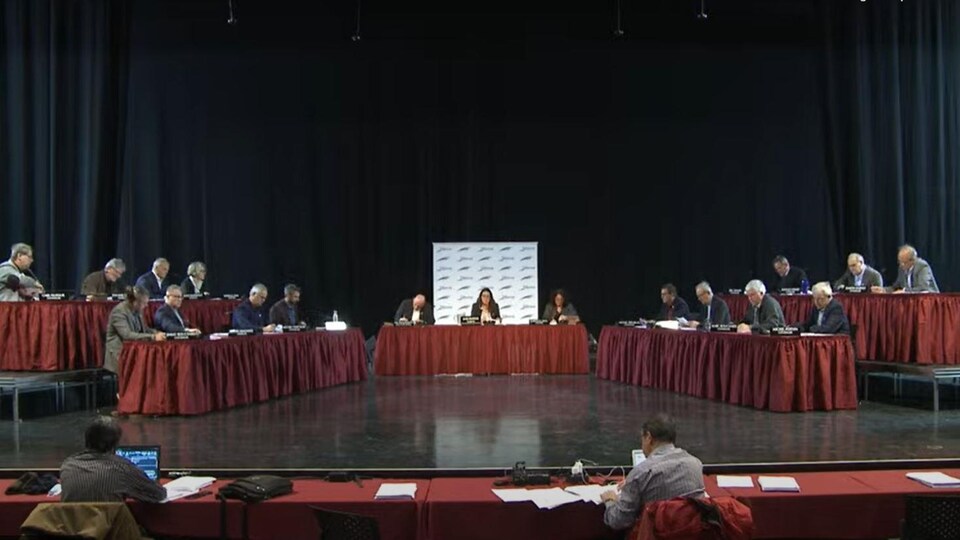 Des conseillers sont assis à deux tables face à face dans une salle.