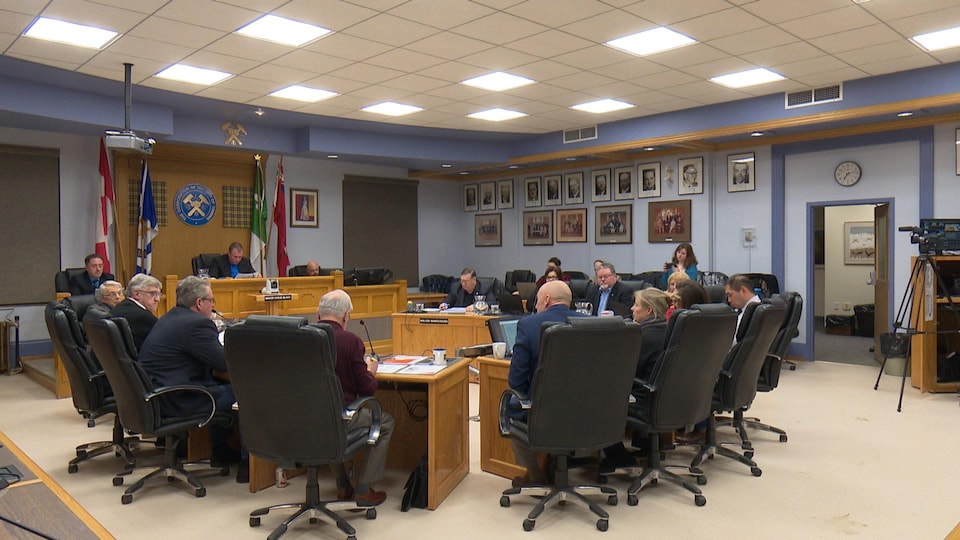 Les conseillers sont assis autour de tables dans la salle de réunion du conseil municipal.