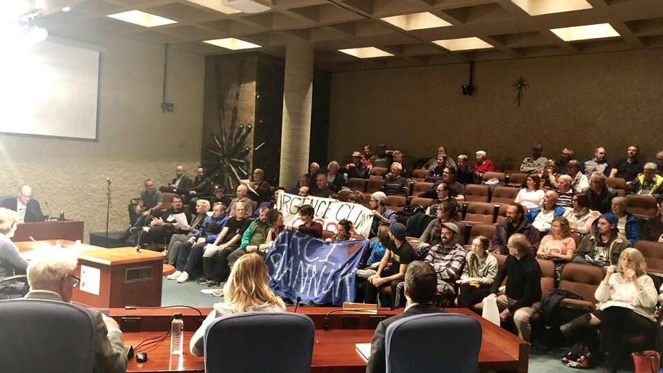 Des citoyens dans les sièges de la salle du conseil municipal avec des banderoles où on peut lire notamment : urgence climatique.