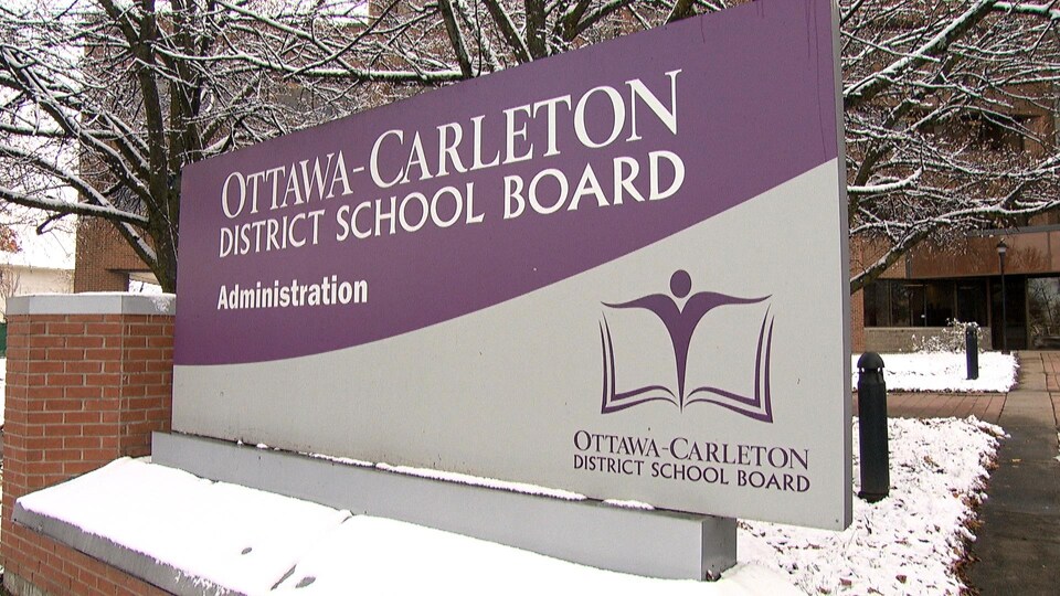 Un écriteau annonce le Conseil scolaire du district d’Ottawa-Carleton, devant un immeuble situé dans un paysage enneigé.