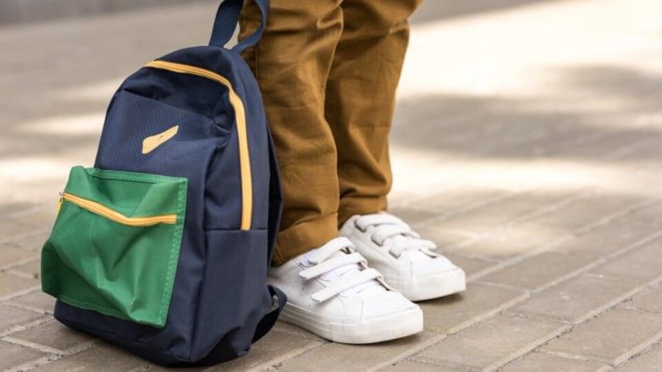 Des chaussures blanches d'enfants, avec un sac à dos à côté.