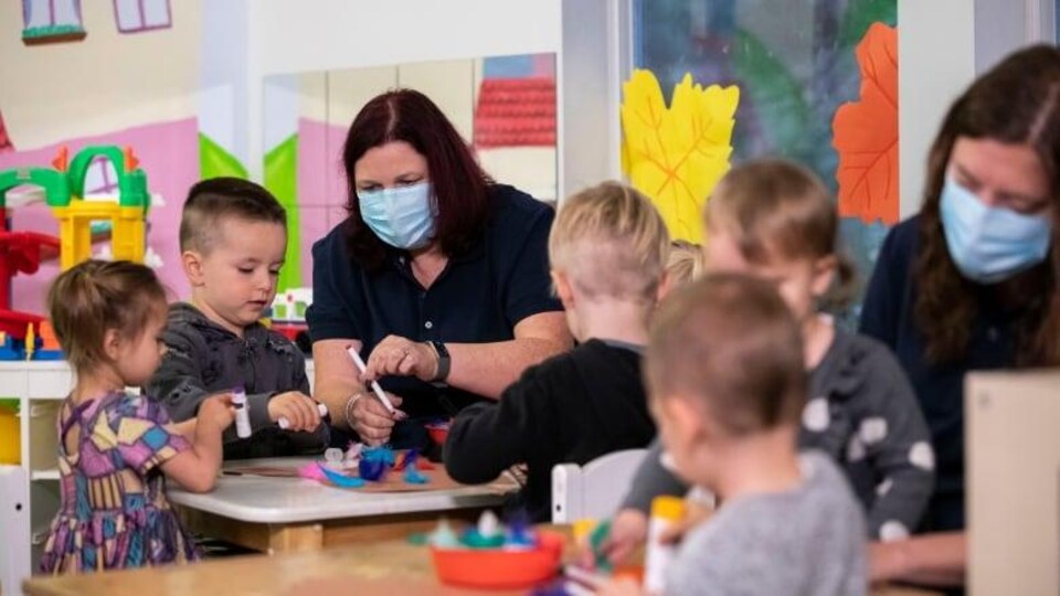 Des enfants dessinent à une table avec une enseignante dans une classe de maternelle.