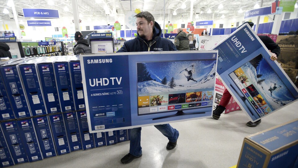 Un homme transporte un téléviseur dans un commerce.