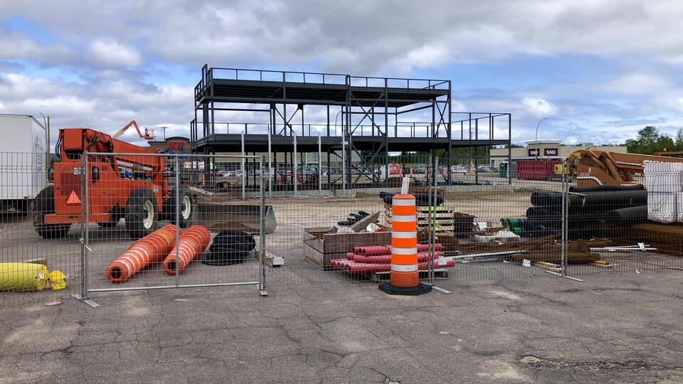 Un chantier de construction vide, entouré de clôture et de cônes oranges.