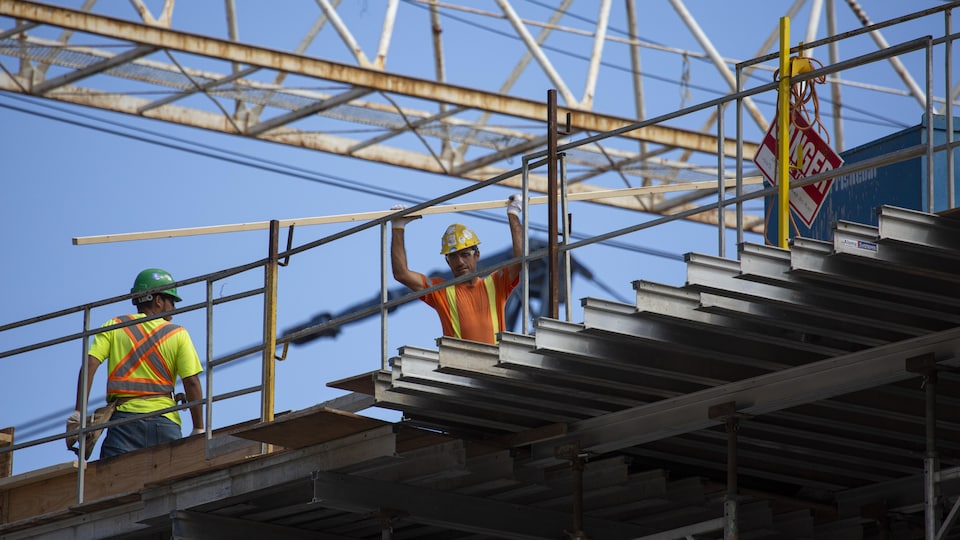 Des ouvriers sur un édifice en construction, avec une grue en arrière-plan.