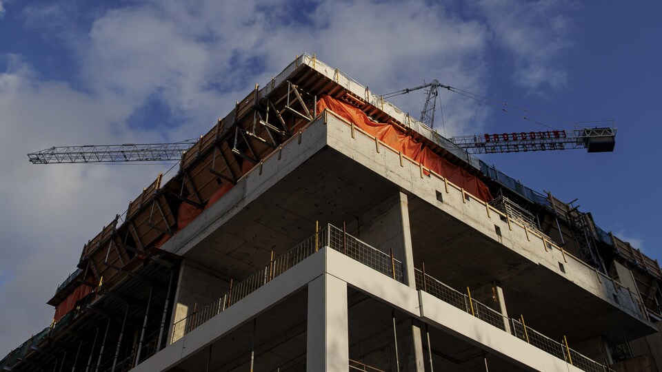 Une grue surmonte un immeuble à appartements en construction.