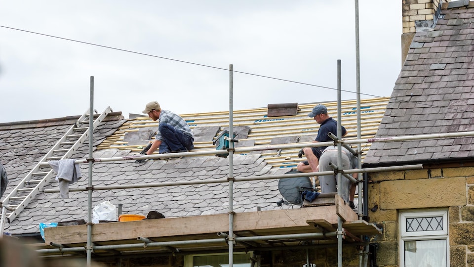 Trois travailleurs changent la toiture d'une maison.