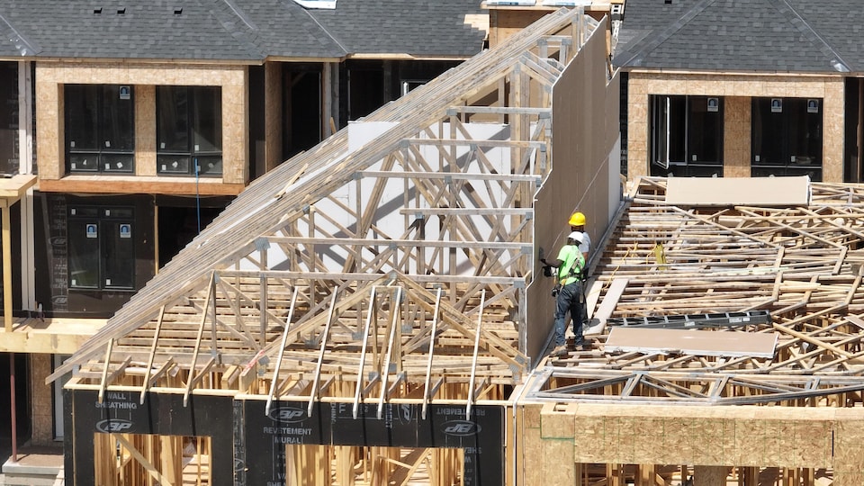 Deux ouvriers assemblent le toit d'une maison sur un chantier.