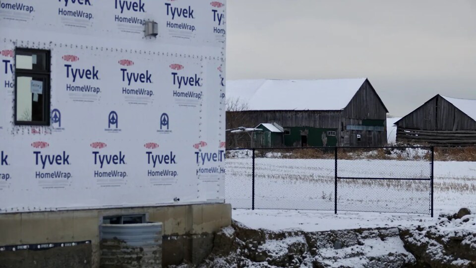 Des logements en construction en hiver, avec au loin des fermes.