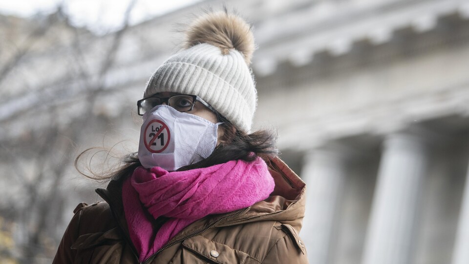 Une femme porte un masque sur lequel est imprimé un symbole contre la loi 21.
