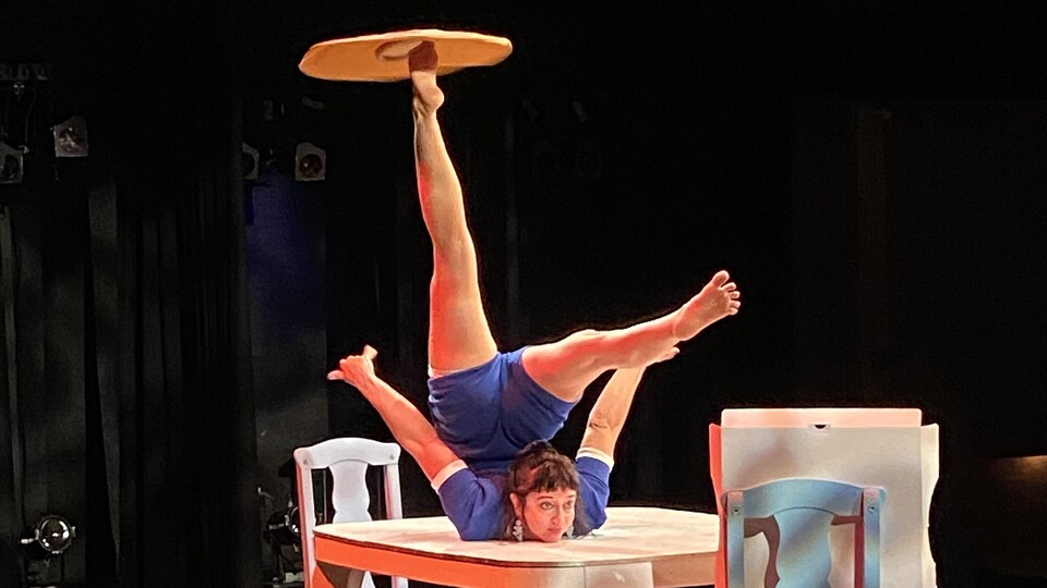 Une contorsionniste sur une table fait tourner une pizza sur son pied.