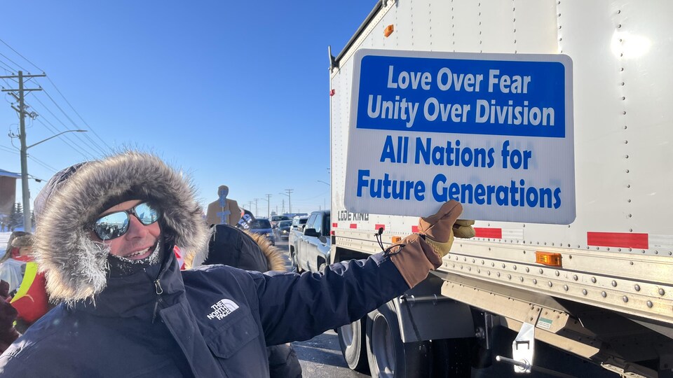 Un homme montre une affiche appelant à l'unité alors qu'il se trouve à côté d'un camion qui circule sur la transcanadienne.