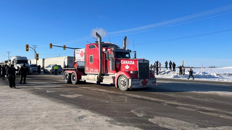 Un camion rouge en avant-plan roule sur la transcanadienne à Headingley, alors que des gens se trouvent dans l'accotement.