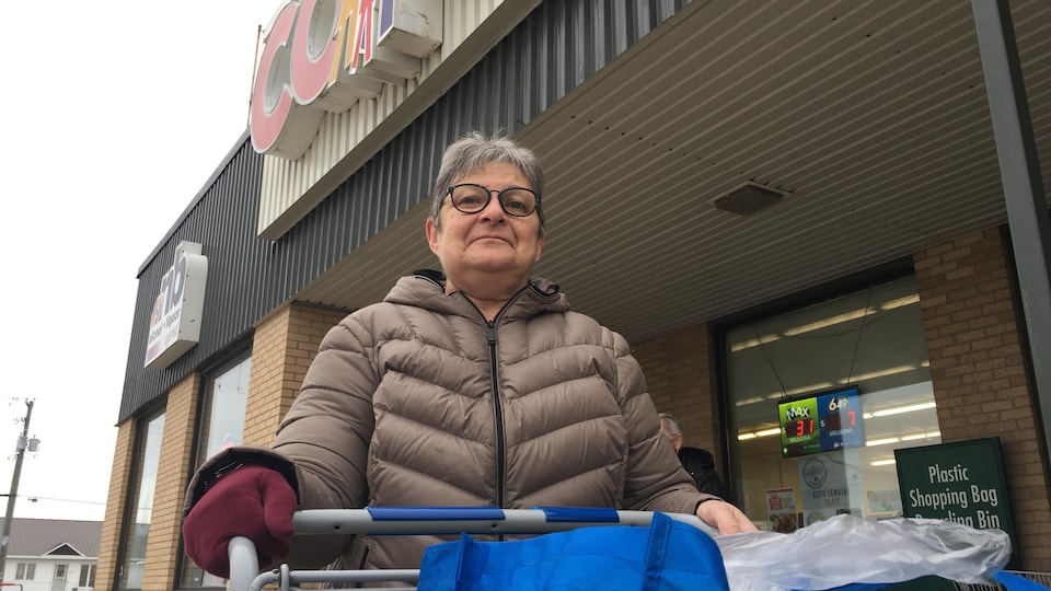 Un femme sortant d'une épicerie avec son panier de provisions.