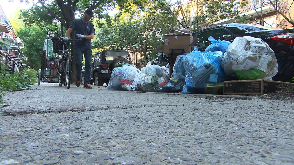 Un homme avec son vélo regarde les sacs de recyclage déposés par terre à la recherche de canettes ou de bouteilles consignées. 