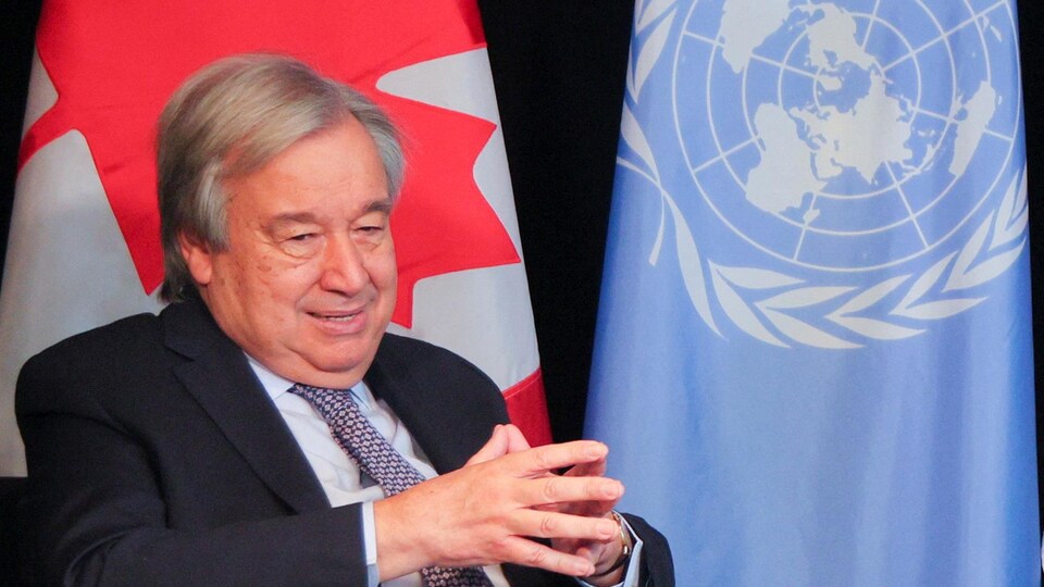António Guterres sourit devant les drapeaux du Canada et de l'ONU.