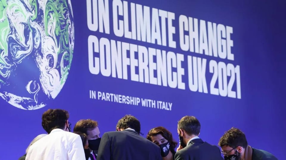 Des participants à la COP 26 se concertent, et derrière eux se trouve l'affiche du sommet.
