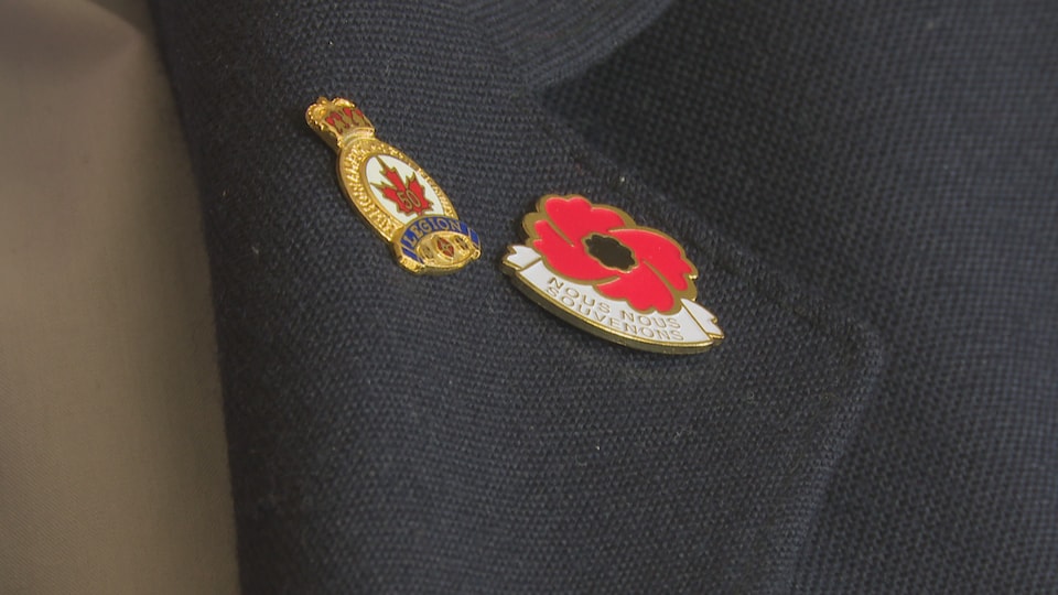 Un insigne en forme de coquelicot est attaché sur le veston de Réginald Basque. Il est écrit: "Nous nous souvenons".