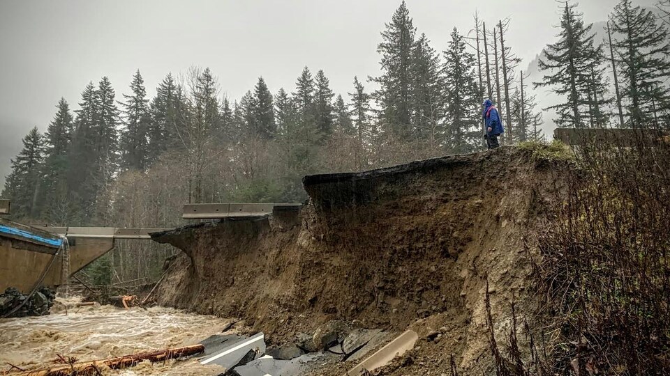 Un personne regarde la destruction d'une portion de la route Coquihalla.