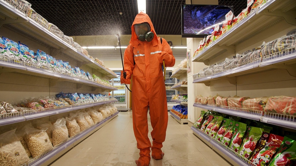 Un homme en combinaison de protection vaporise un produit désinfectant dans les allées d'une épicerie. 
