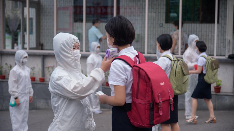 A woman wearing a protective suit takes a student’s temperature.