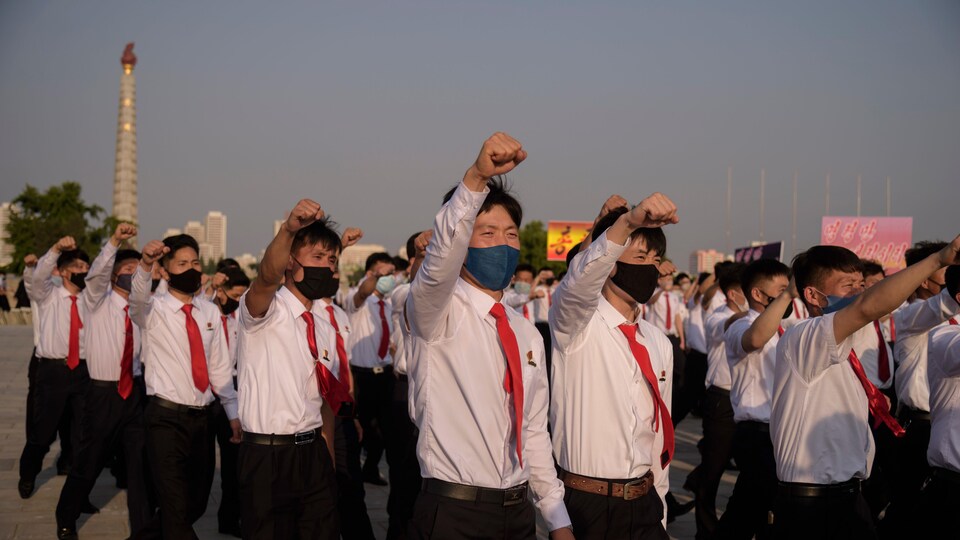 Masquées, des dizaines de garçons défilent, tous vêtus d'une chemise et d'une cravate, le poing droit en l'air.