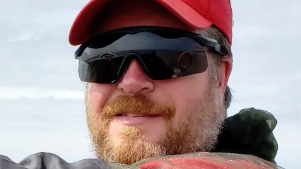 Corey Hurren, portant une casquette et des lunettes de soleil, regarde la caméra.
