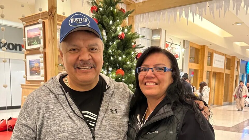 Le couple est souriant devant un arbre de Noël.