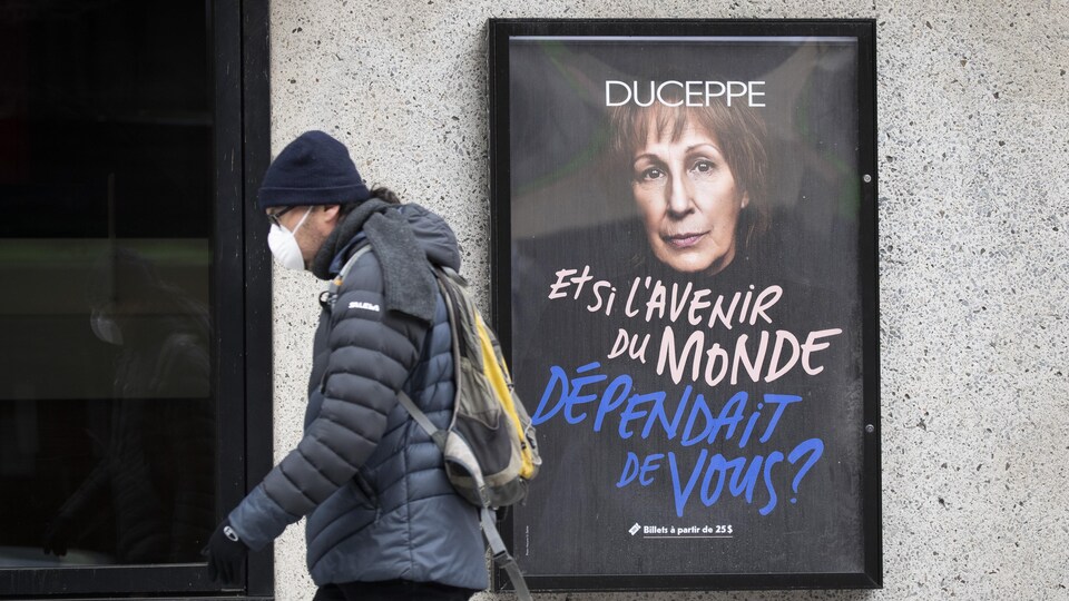Un passant masqué passe devant une affiche.