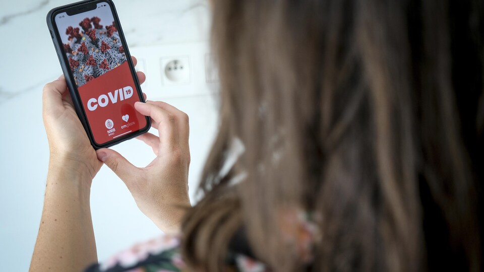 Une femme manipule un téléphone intelligent avec une application de traçage de la COVID-19 à l'écran.